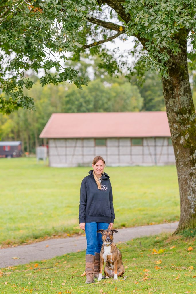 Kathrin steht mit einem Hund im Grünen